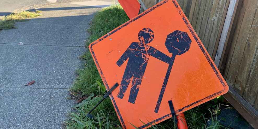 A road construction sign leans against a fence.