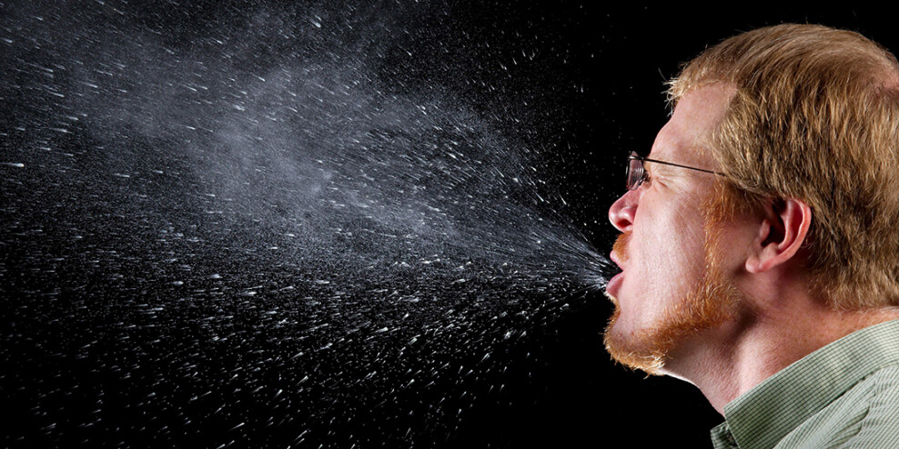 A man sneezes on a black background so you can see all the spit droplets.