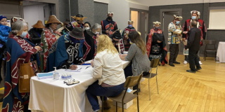 A group of people in traditional dress gather behind a table in a community centre.