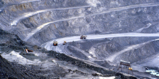 A wide view of the inside of an open pit copper mine. The huge dump trucks look tiny in the mine.