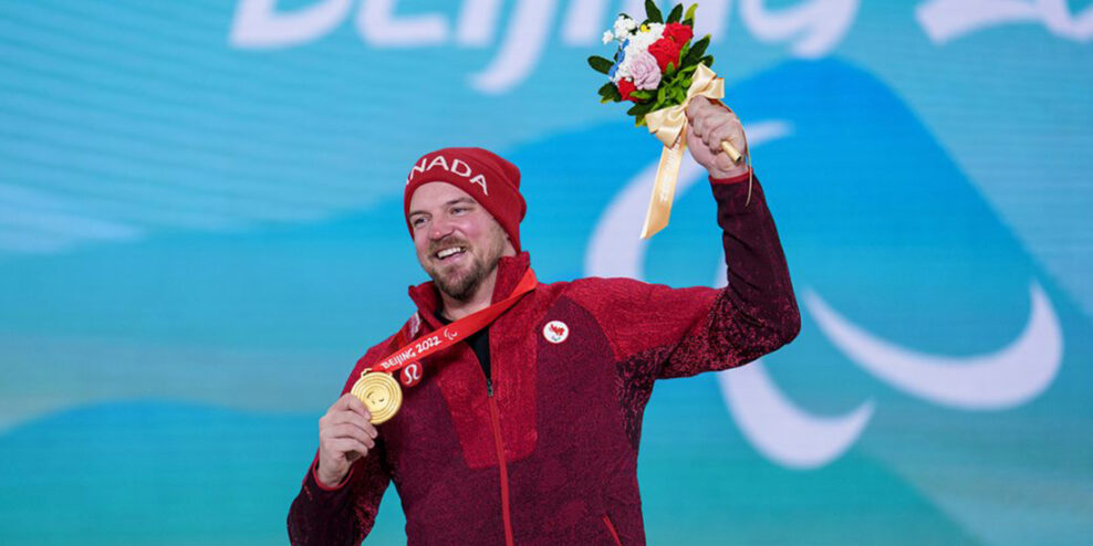 Tyler Turner raises a bouquet of flowers and holds up his gold medal. He has a huge smile on his face.