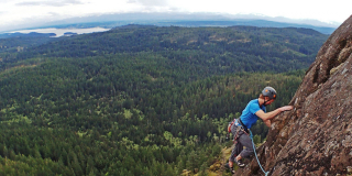 Philip Stone climbs a crag with a view of the Georgia Strait behind him.