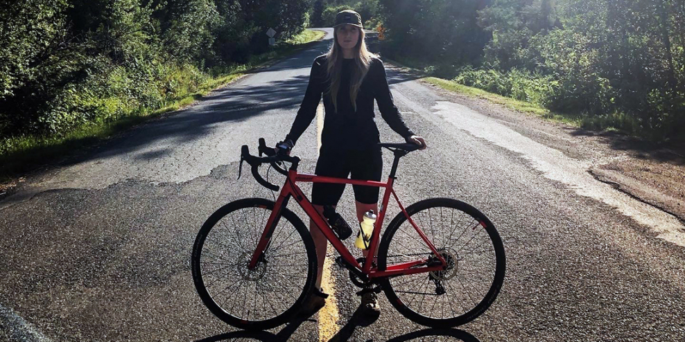 Alexandra Vallée stands with her bike on a winding road.