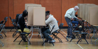 Rows of voting booths, but with only three or four of the booths have a person in them.