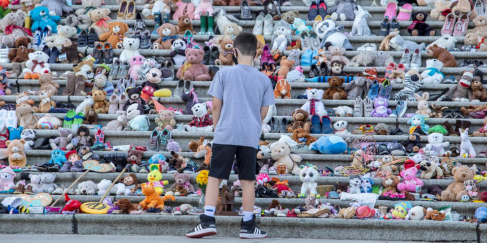 A child stands in front of rows of teddy bears left on the Victoria legislature steps.