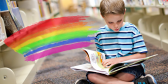 A child sits crosslegged on a library floor reading between stacks of books.