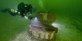 A scuba diver swims near a port in the top of a sunken ship.