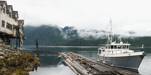 A small fishing boat is moored at a decaying dock next to a crumbling building on stilts.